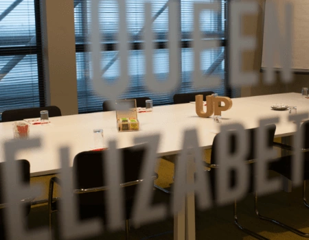 Vergaderruimte met lange tafel en stoelen, gezien door glas waarop 'Queen Elizabeth' staat.