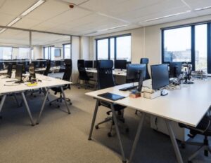 Moderne, open kantoorruimte met meerdere lege werkplekken en bureaustoelen.