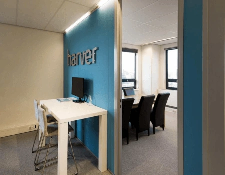 Moderne vergaderruimte bij Harver met een blauwe accentmuur, hoge tafel met stoelen en een aparte vergaderkamer met conferentiestoelen.