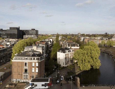 Luchtfoto van een groene stadsstraat in Amsterdam met grachten en historische gebouwen.