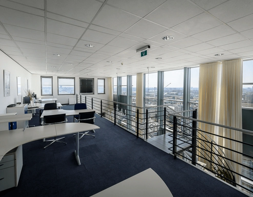 Modern kantoor op een bovenverdieping met bureaus, bureaustoelen en grote ramen met uitzicht op de stad.
