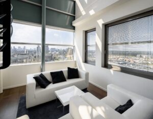Modern ingericht kantoor met witte banken en uitzicht op de skyline van een stad door grote ramen.