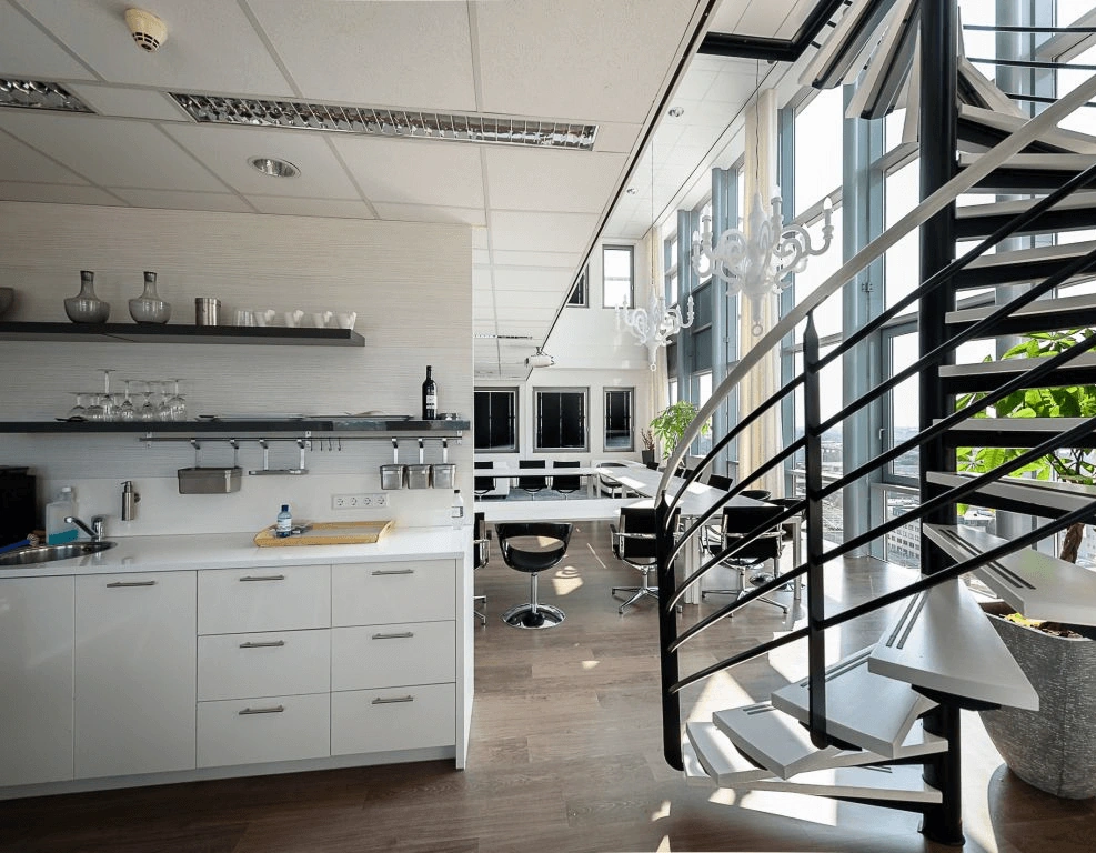 Moderne kantoorruimte met een open keuken, design trap en grote ramen die veel daglicht binnenlaten.