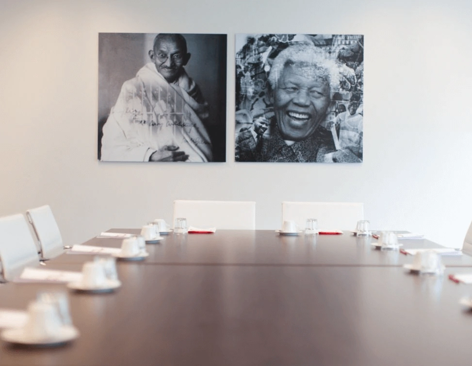 Vergaderruimte met een lange tafel, witte stoelen en twee zwart-wit portretten aan de muur van Mahatma Gandhi en Nelson Mandela.