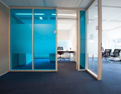 Modern kantoorinterieur met blauwe glazen wanden en vergaderruimte op de achtergrond.
