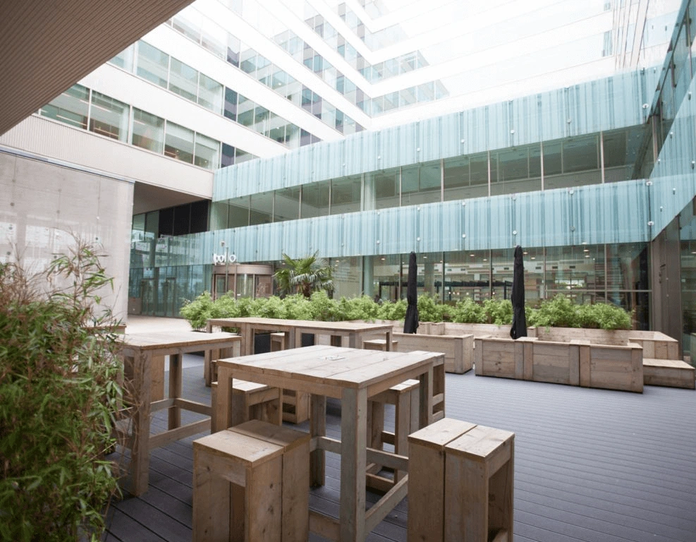 Moderne buitenruimte met houten zitmeubilair en omringd door glazen kantoorgebouwen.
