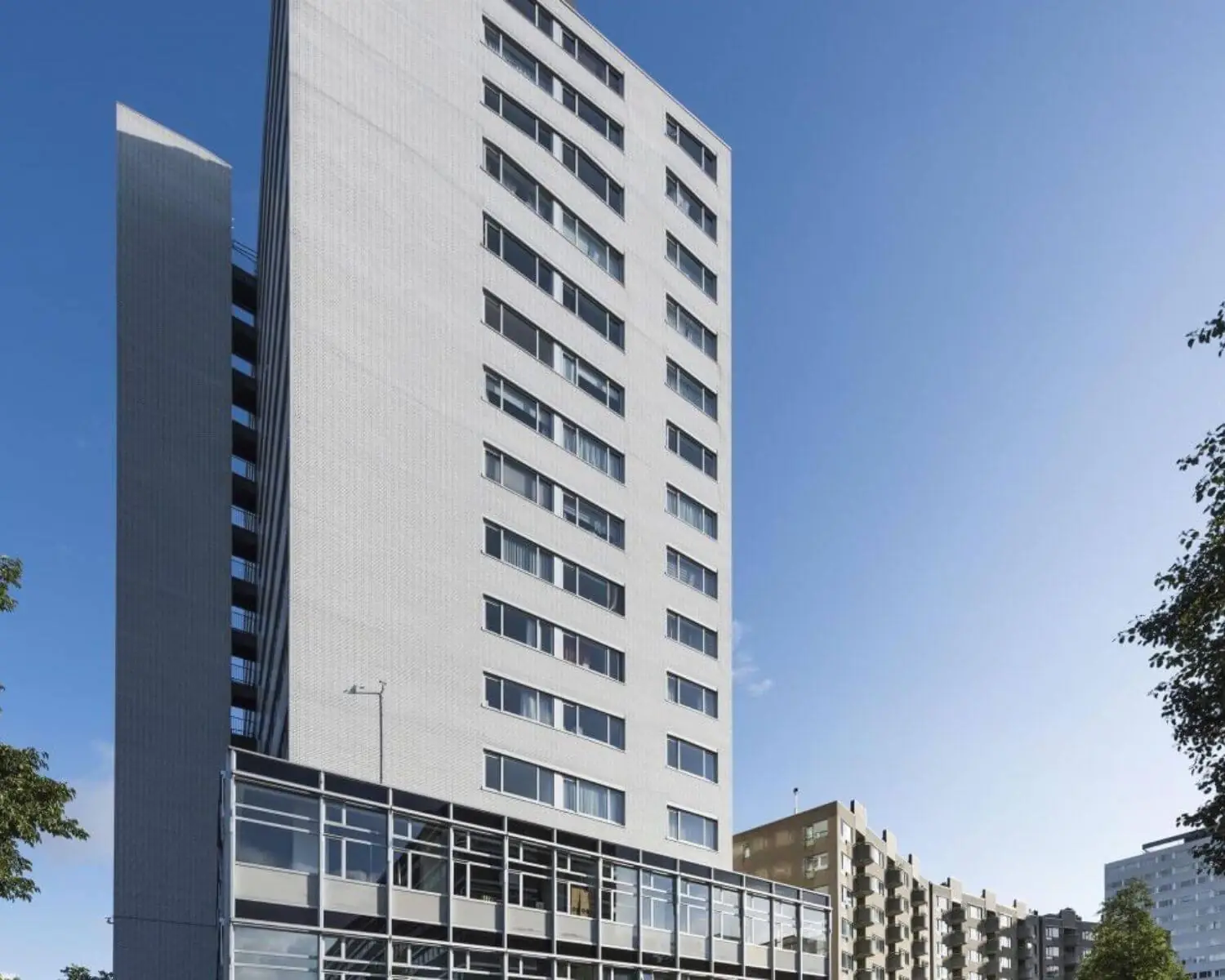 Een modern, wit hoogbouwappartement met grote ramen tegen een blauwe hemel.