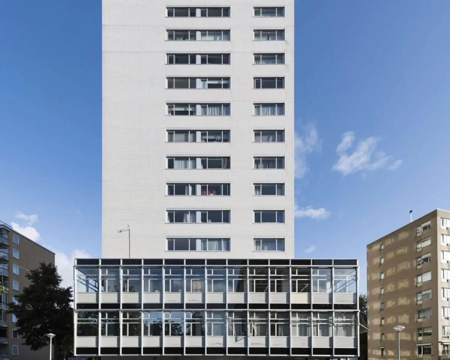 Wit, modern woongebouw met een glazen voorbouw en blauwe lucht op de achtergrond.