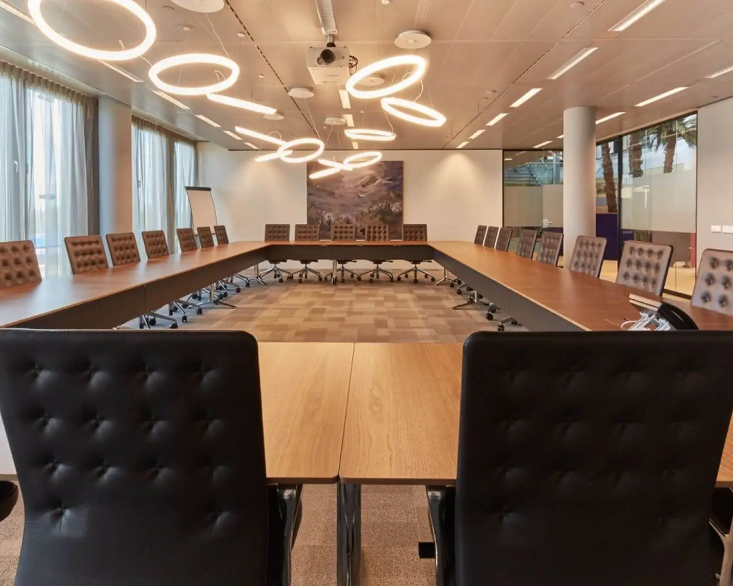 Moderne vergaderruimte met U-vormige opstelling, leren stoelen en opvallende ringvormige plafondverlichting.