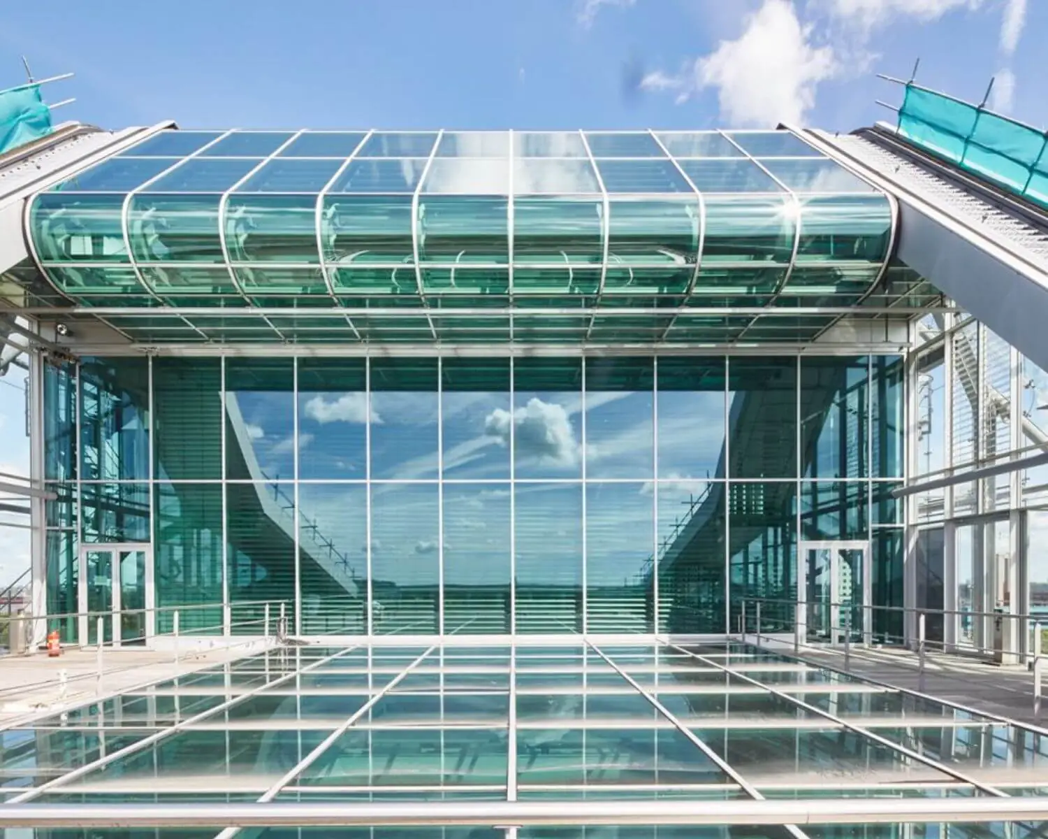 Moderne glazen gevel van een gebouw met symmetrische lijnen en reflecties van de lucht.