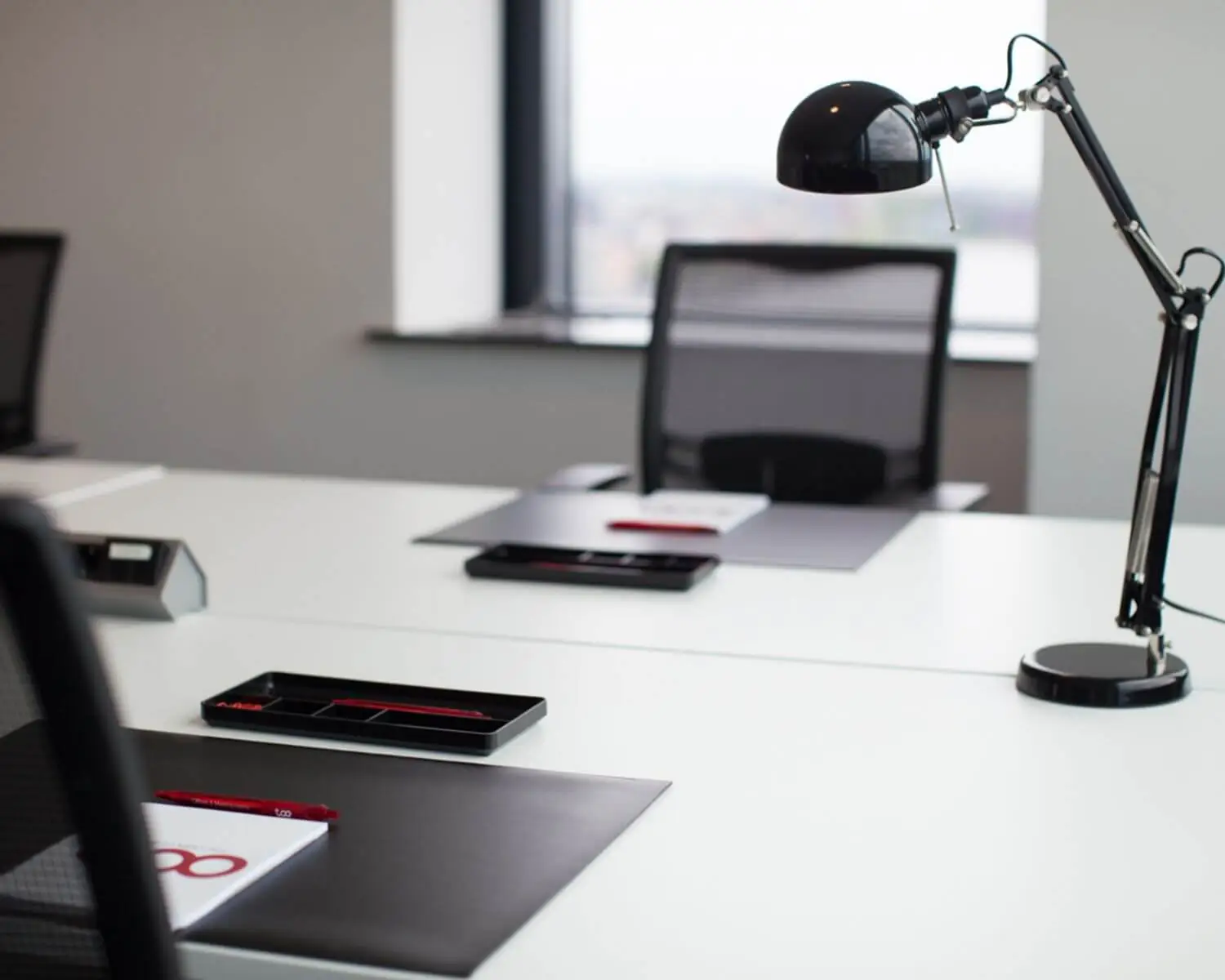 Moderne, minimalistische kantoorruimte met witte bureaus, zwarte stoelen en bureaulampen.