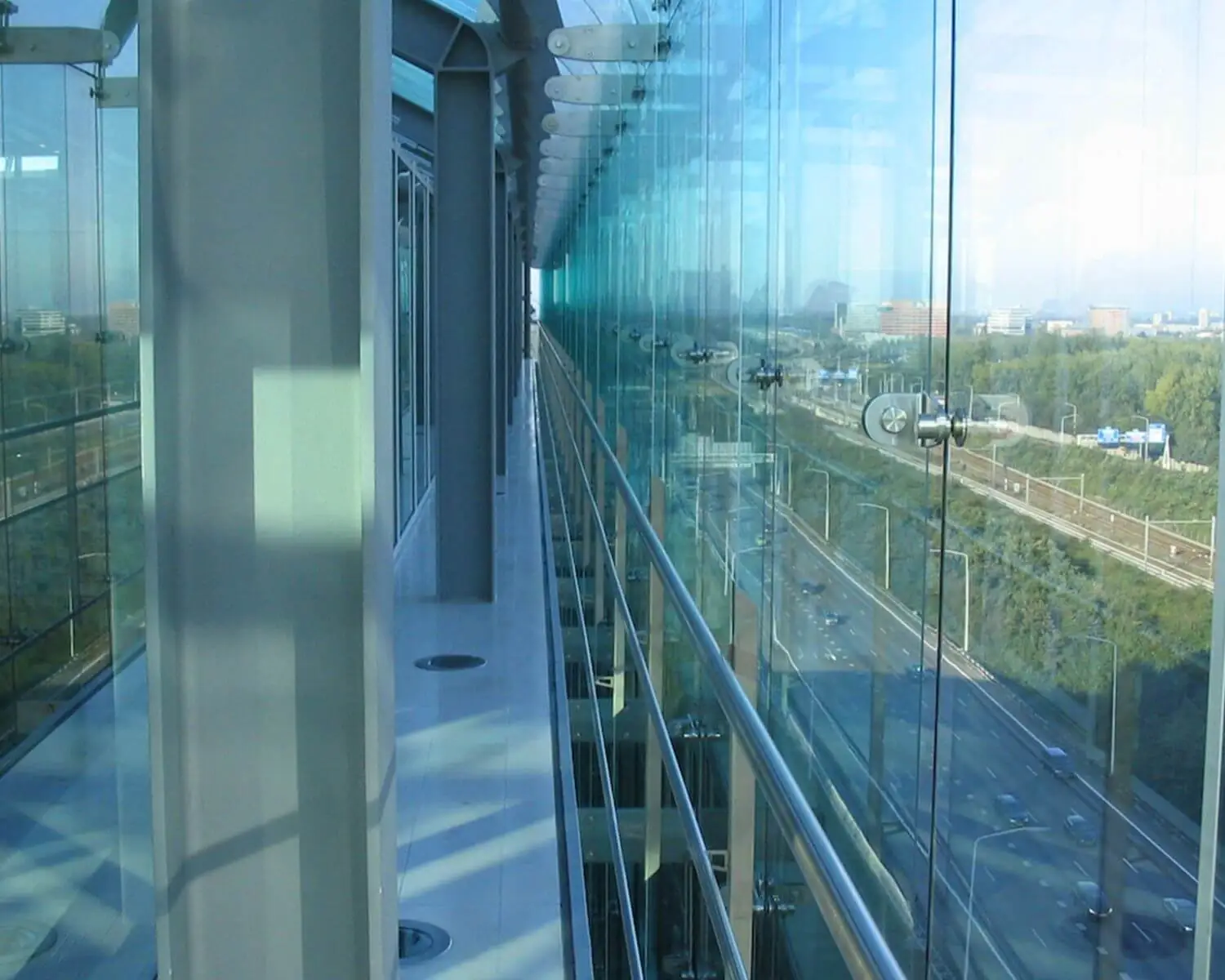 Glazen gevel van een modern kantoorgebouw met uitzicht op een snelweg en stedelijk landschap.