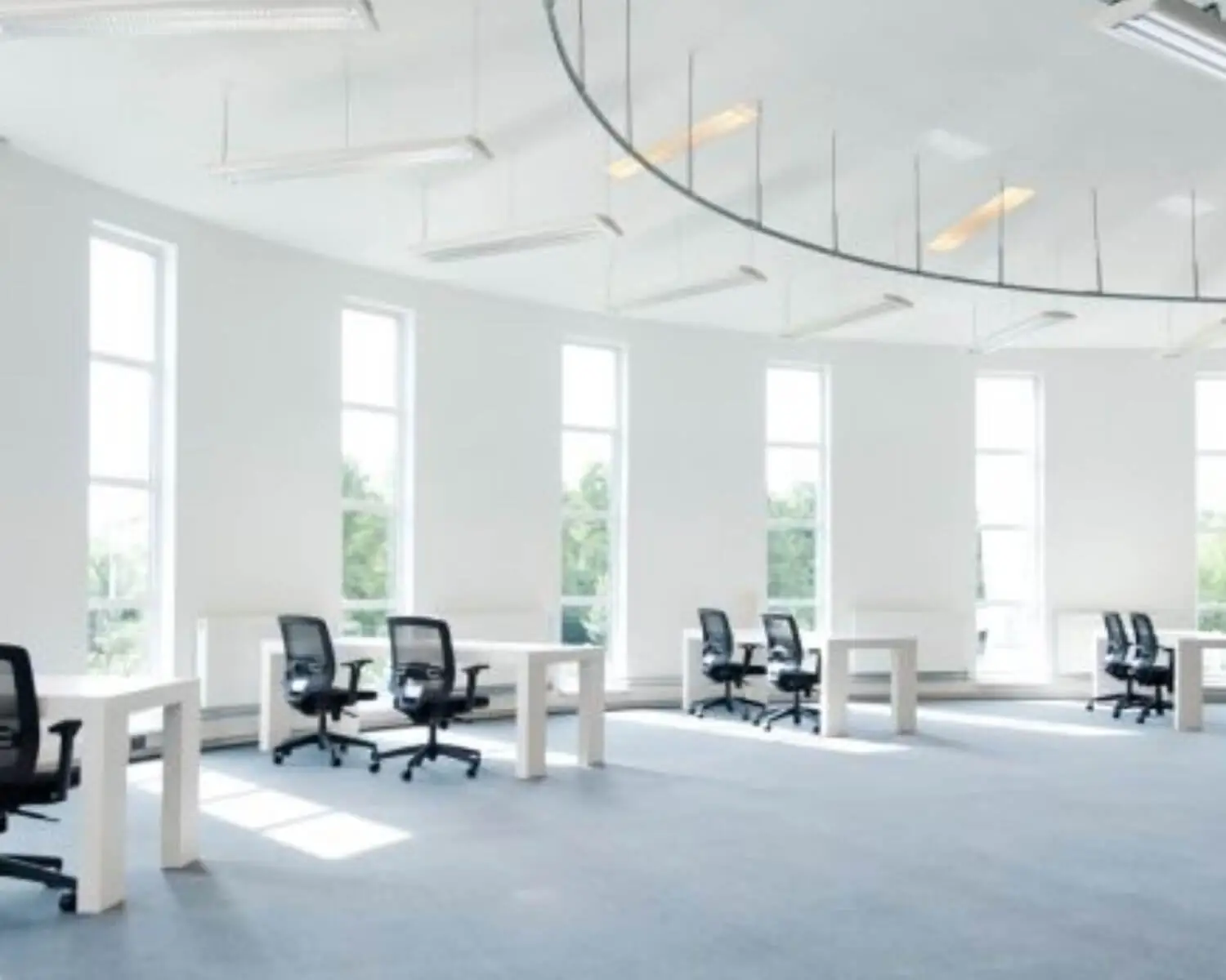 Ruim en licht modern kantoor met witte bureaus en zwarte bureaustoelen bij hoge ramen.