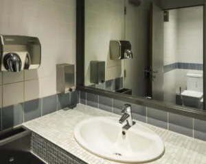 Moderne openbare badkamer met wastafel, grote spiegel, handendroger en zicht op een toilet in de spiegel.