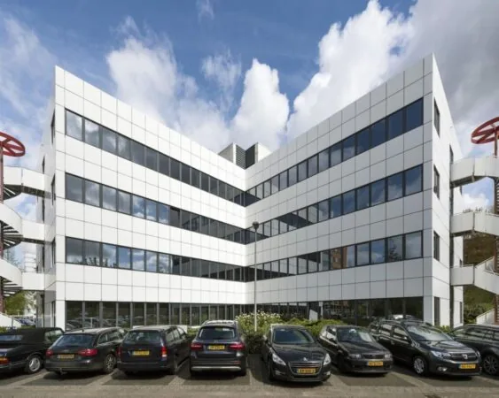 Modern wit kantoorgebouw met spiegelende ramen en geparkeerde auto's op de voorgrond.