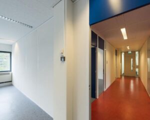 Een leeg kantoor met witte muren en een aangrenzende gang met rode vloer en tl-verlichting.