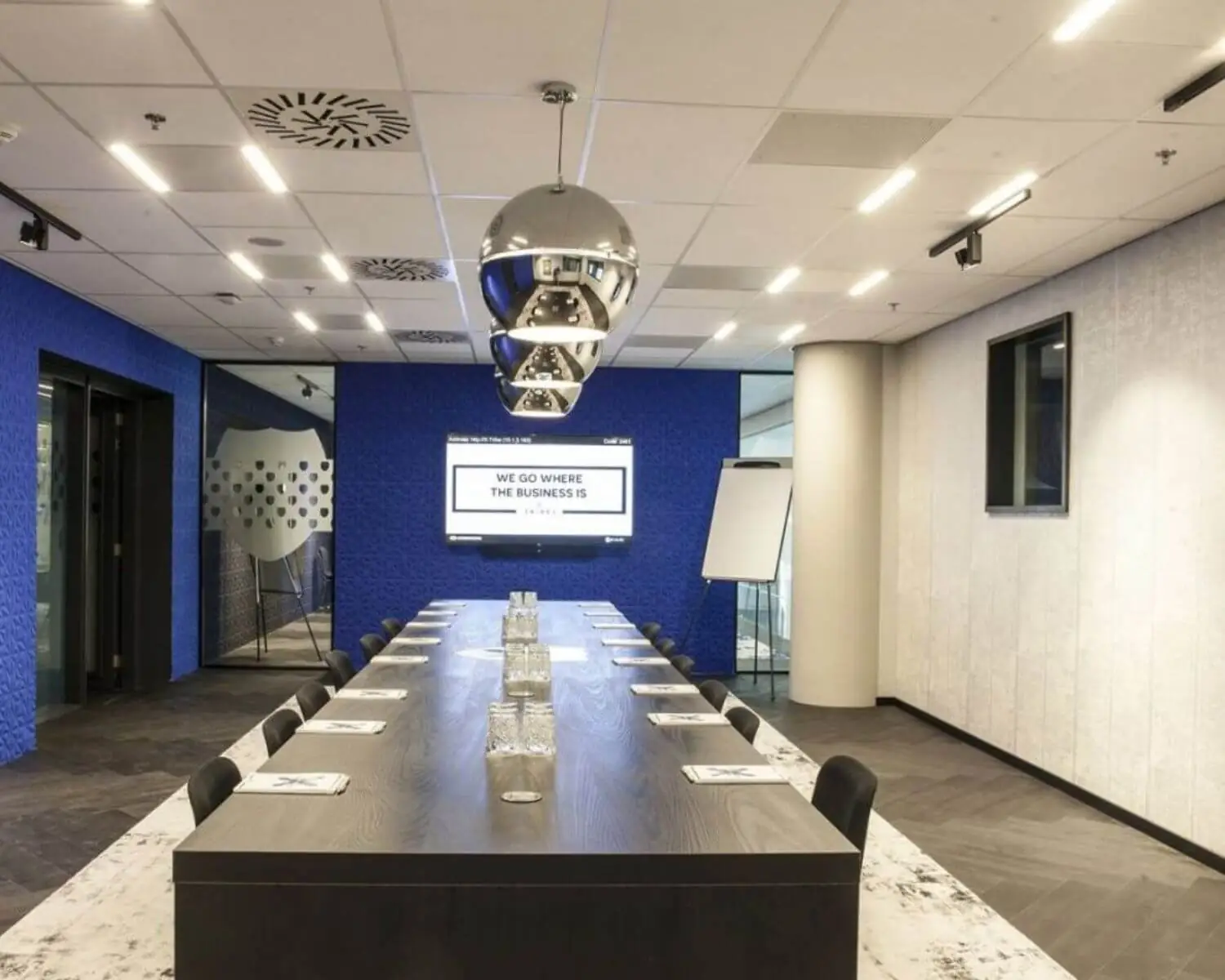 Moderne vergaderzaal met lange tafel, stijlvolle verlichting en een scherm met de tekst "We go where the business is".