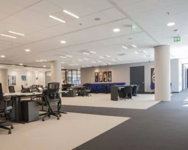 Moderne, open kantoorruimte met bureaus, bureaustoelen, vergadertafels en kunst aan de muur.