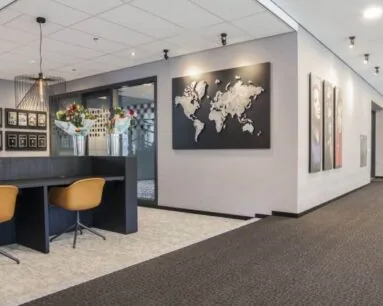 Moderne kantoorruimte met wanddecoratie waaronder een wereldkaart en portretfoto's, en een werkplek met bloemen op het bureau.