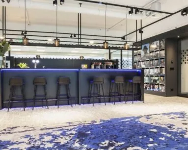 Moderne kantoorbar met hoge zwarte krukken, blauwe LED-verlichting en een wand vol tijdschriftcovers.