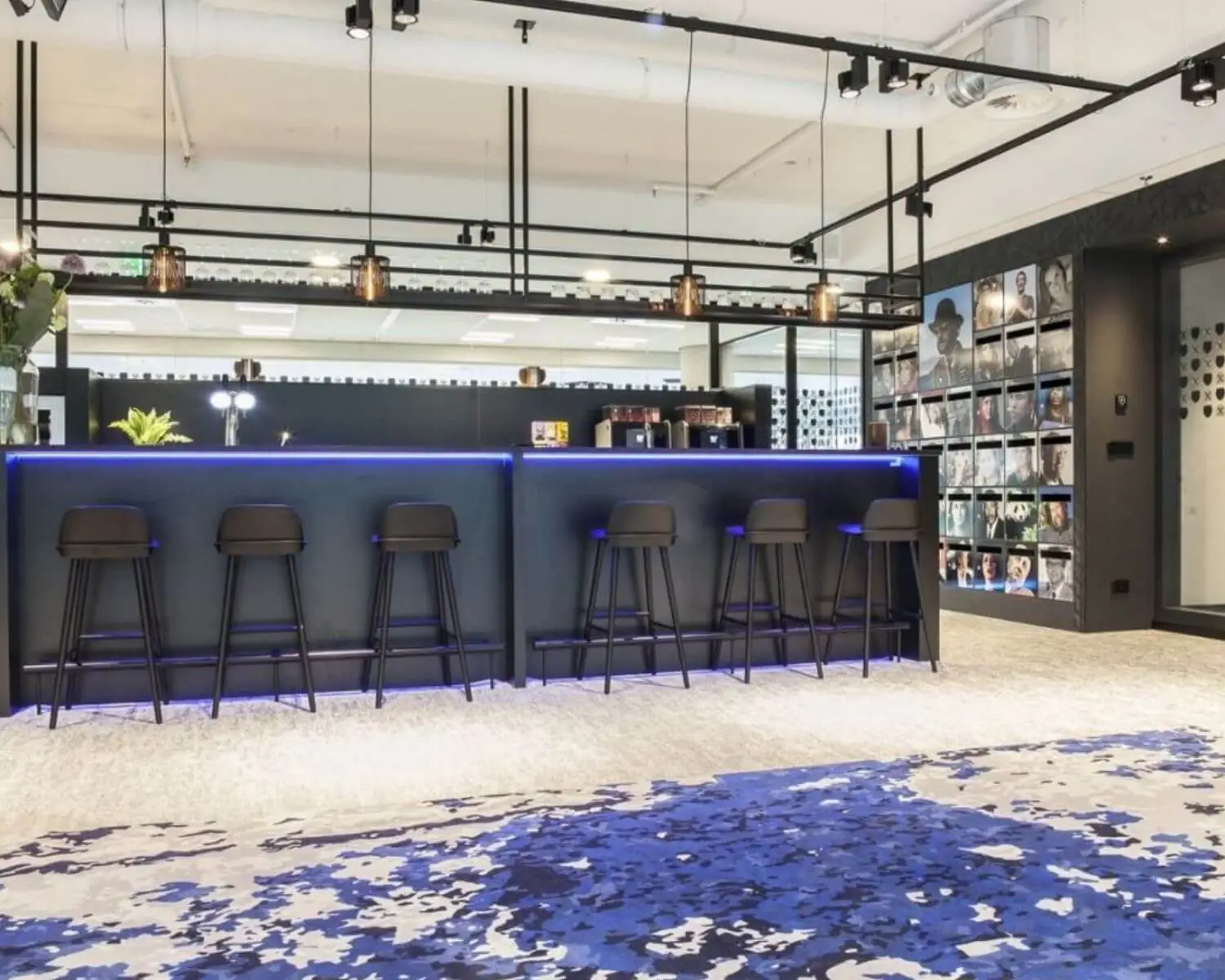Moderne kantoorbar met hoge zwarte krukken, blauwe LED-verlichting en een wand vol tijdschriftcovers.