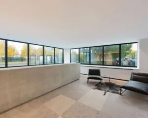 Moderne wachtruimte met grote ramen, betonnen balie, leren meubels en uitzicht op een stedelijke omgeving.