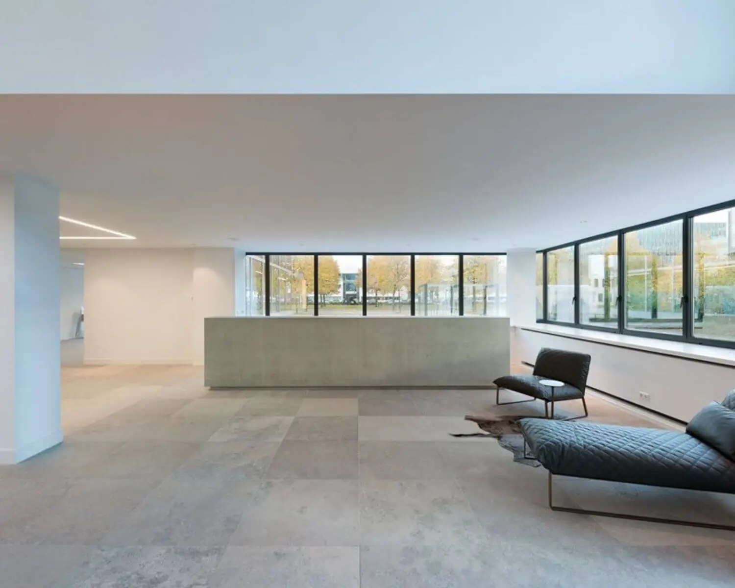 Moderne, minimalistische wachtruimte met grote ramen, betonnen balie en designmeubilair.