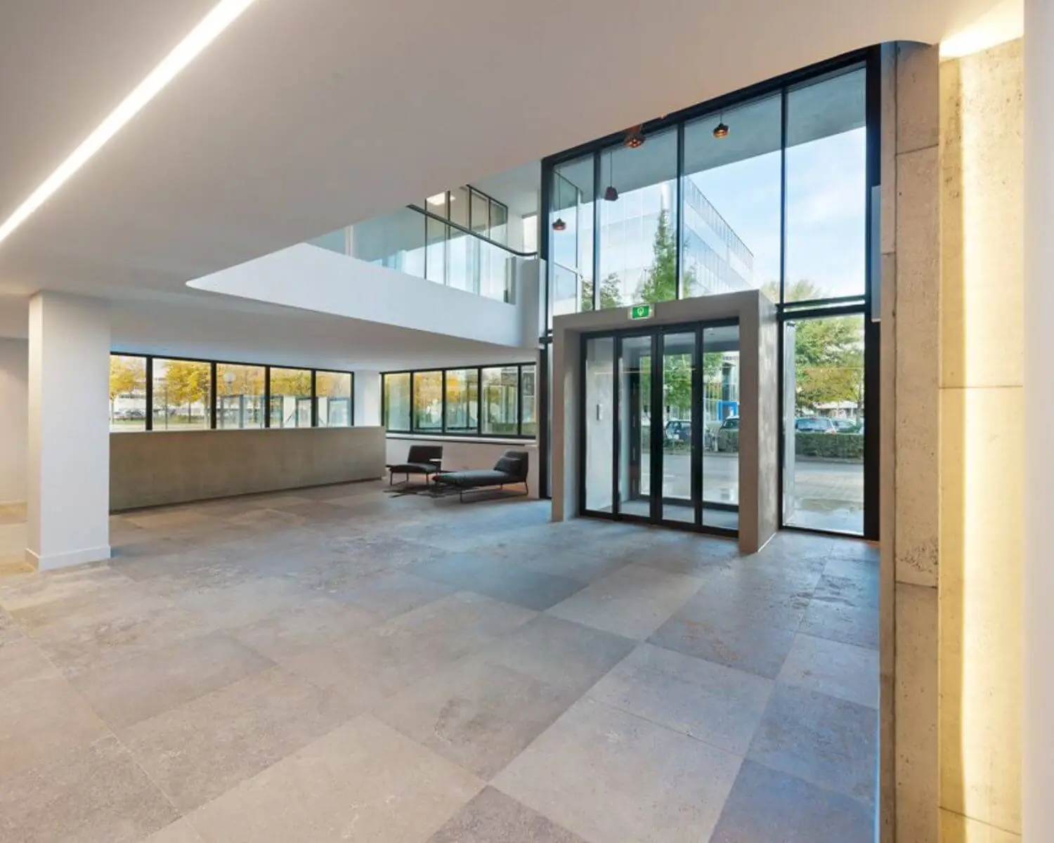 Moderne en lichte entreehal met grote ramen, glazen draaideur en minimalistisch interieur.