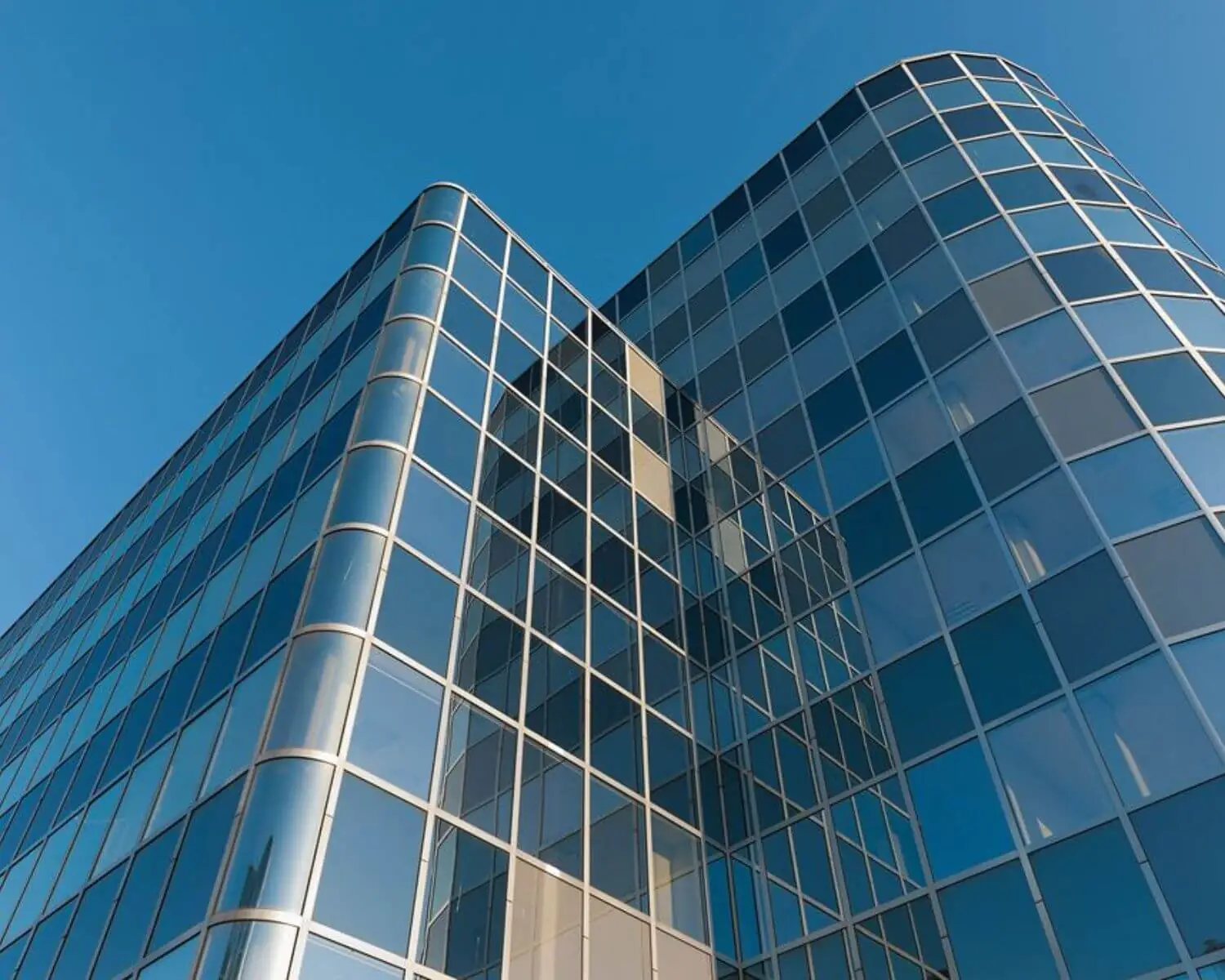 Glazen gevel van een modern kantoorgebouw tegen een heldere blauwe lucht.