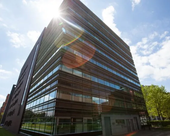 Modern kantoorgebouw met glazen gevels in zonlicht tegen een blauwe lucht.