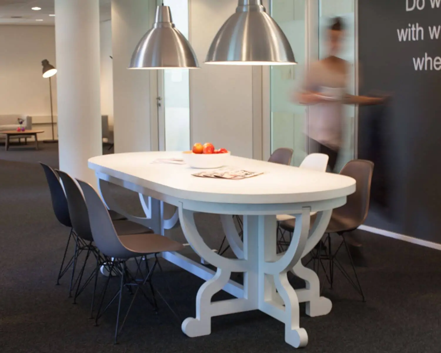 Witte vergadertafel met moderne zwarte en witte stoelen in een kantoorruimte, met een fruitschaal en tijdschriften erop.