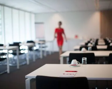 Een moderne vergaderruimte met opgestelde tafels, een notitieboekje en een vrouw in een rode jurk op de achtergrond.