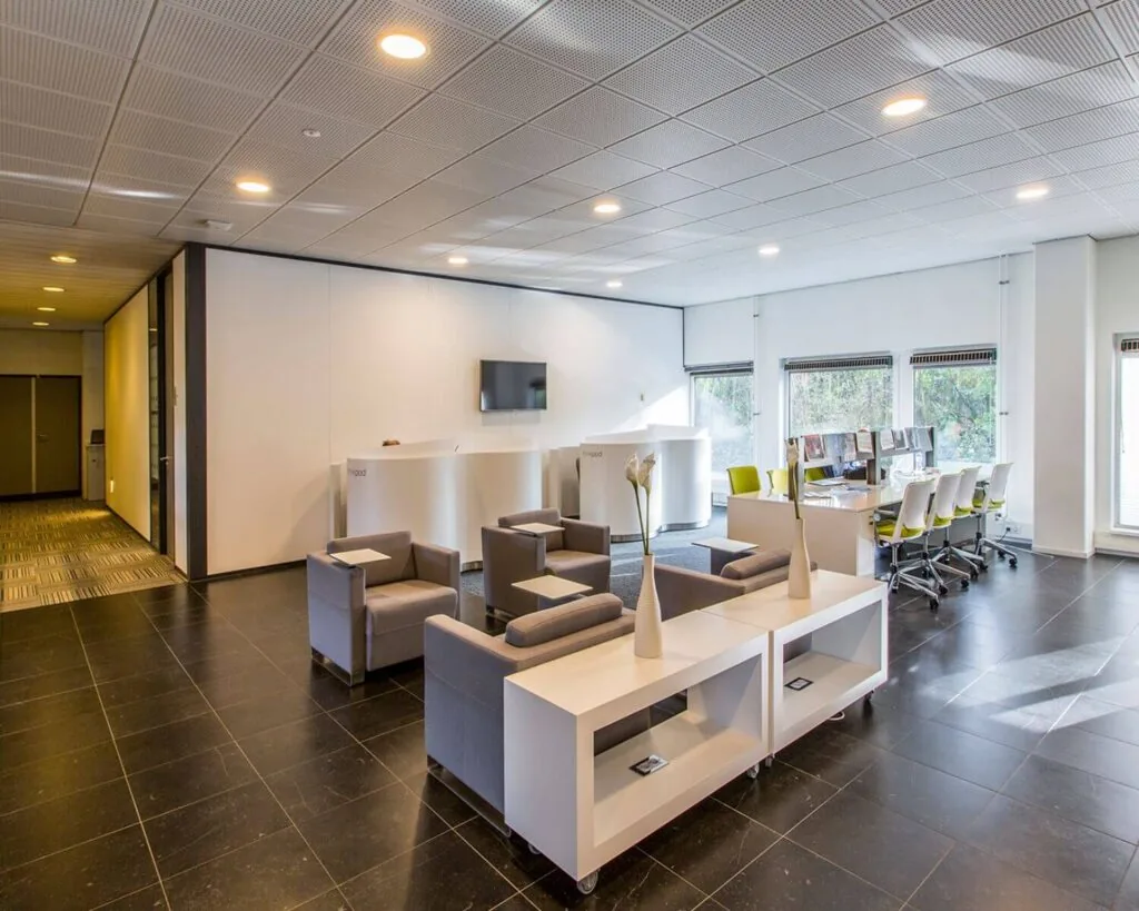 Moderne kantoorruimte met een wachthoek en werkplekken bij grote ramen.