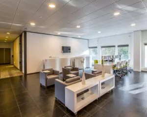 Moderne kantoorruimte met een wachthoek en werkplekken bij grote ramen.