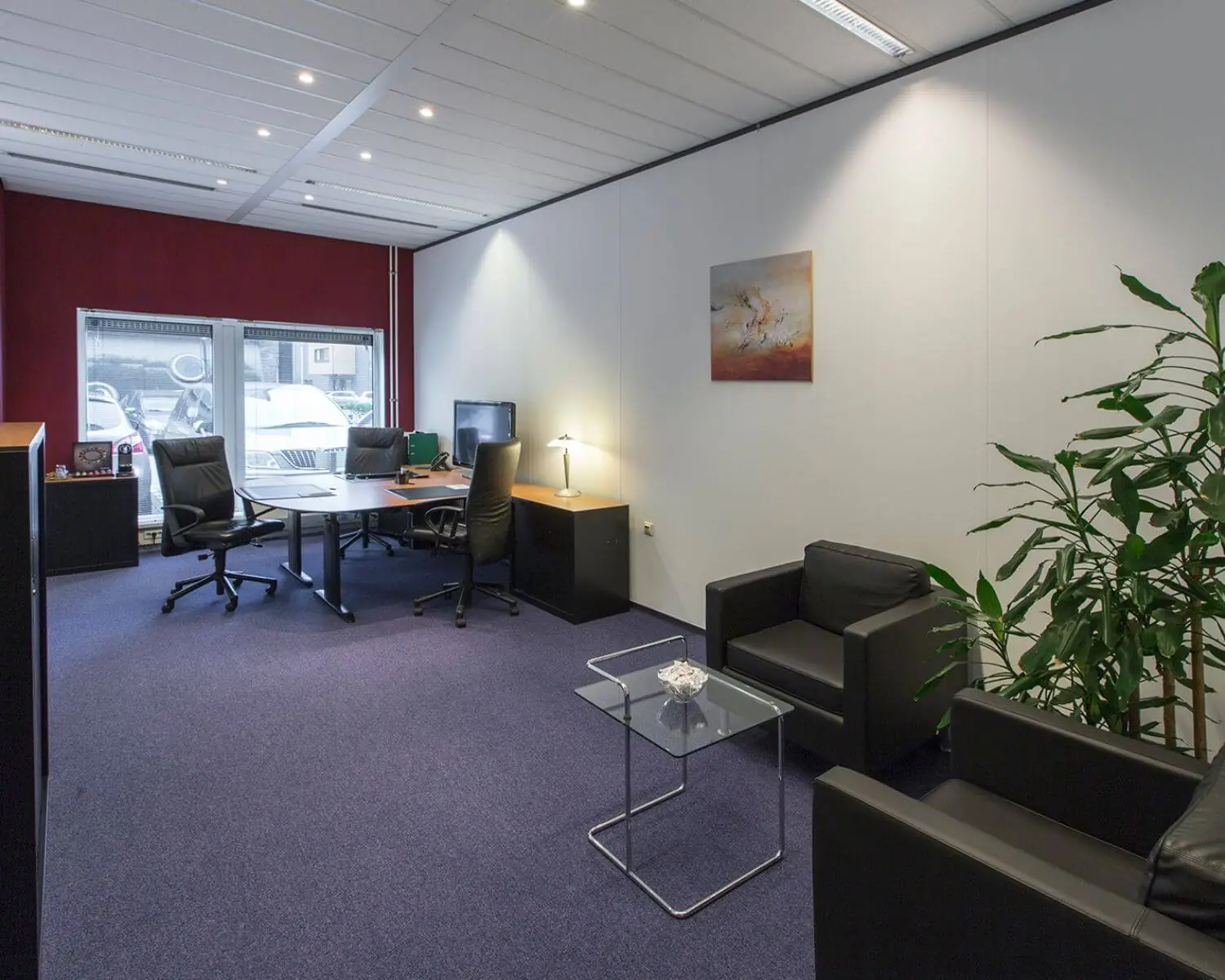 Modern kantoor met bureau, vergaderstoelen, zithoek en een grote plant in een strak ingerichte ruimte.