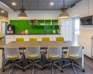 Moderne kantineruimte met groene accenten, een lange tafel en acht bureaustoelen.