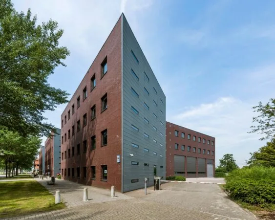 Modern hoekgebouw met een opvallende gevelcombinatie van rood baksteen en grijze panelen, gelegen aan een rustige straat met bomen.