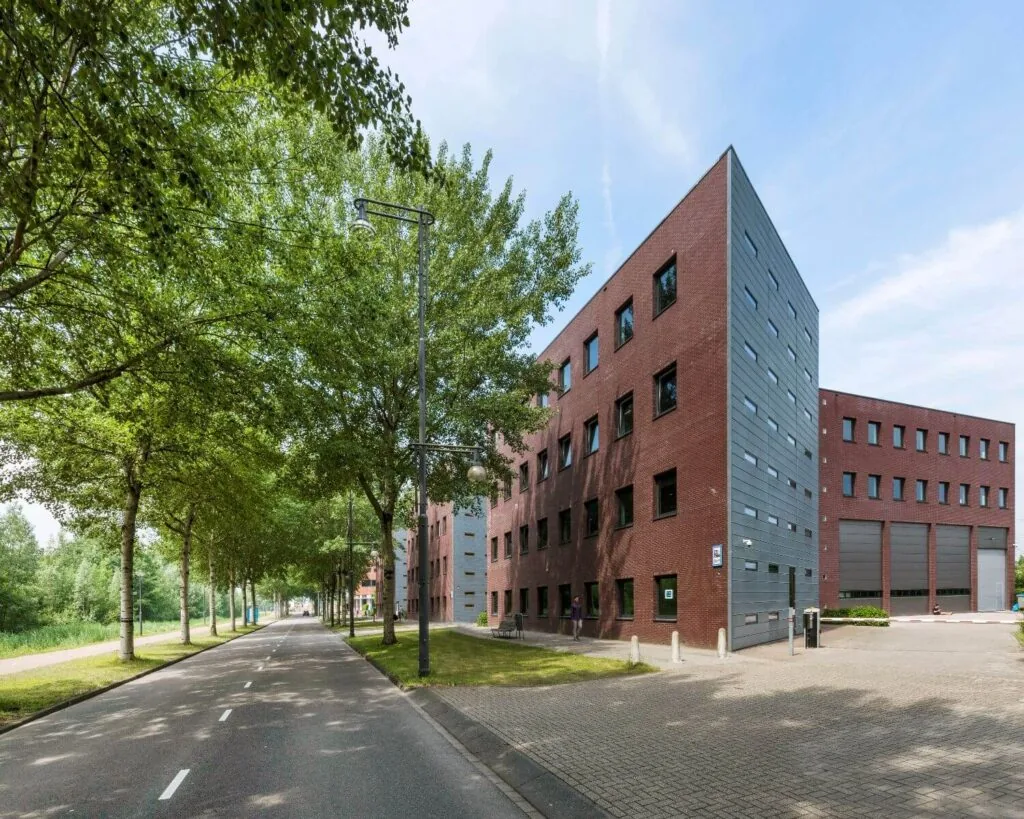 Modern rood bakstenen kantoorgebouw met grijze accenten aan een boomrijke straat.