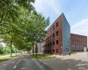 Modern rood bakstenen kantoorgebouw met grijze accenten aan een boomrijke straat.
