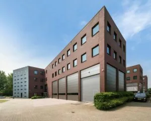 Modern bedrijfsgebouw met rode bakstenen gevel, grote ramen en meerdere grijze roldeuren.