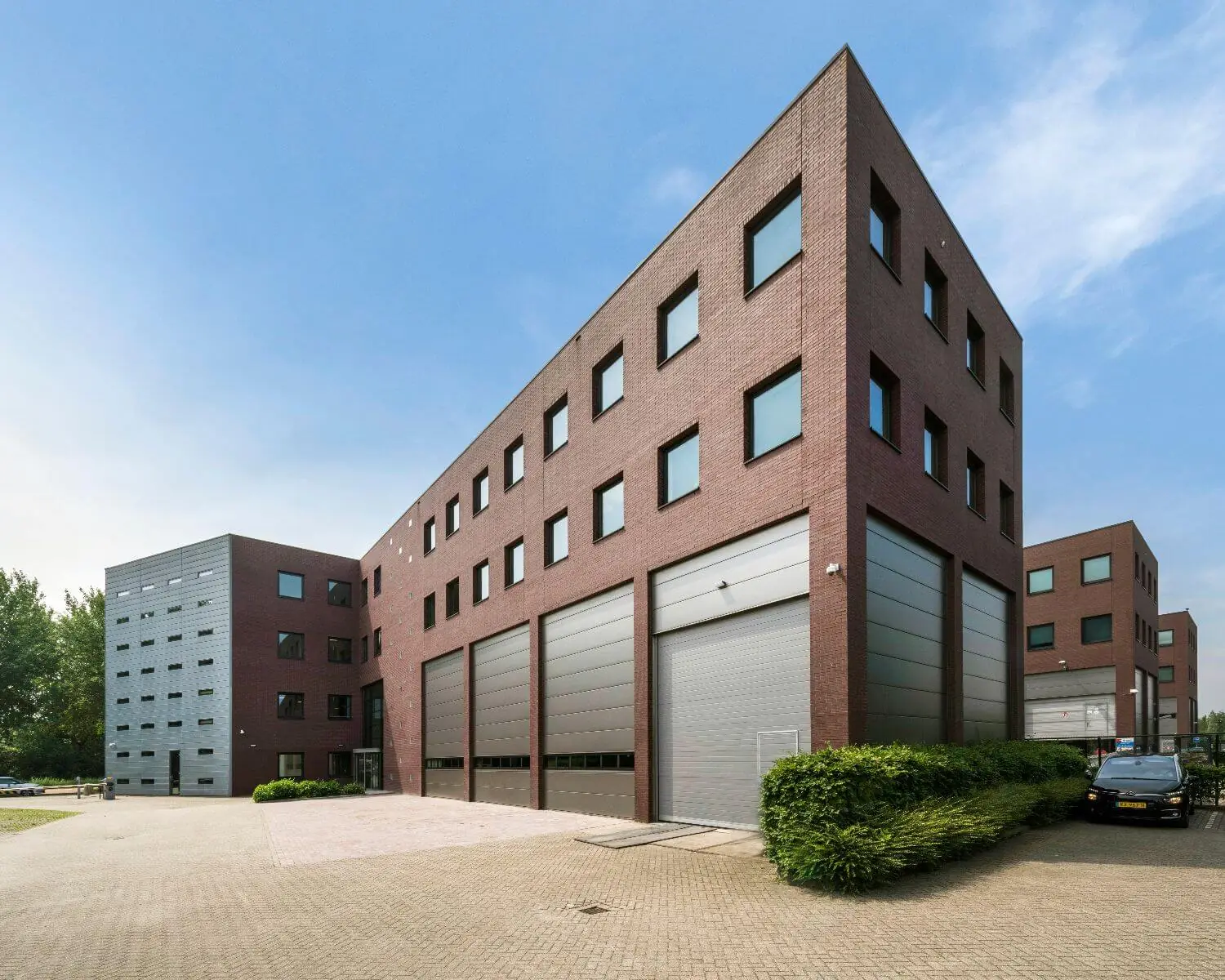 Modern bedrijfsgebouw met rode bakstenen gevel, grote ramen en meerdere grijze roldeuren.
