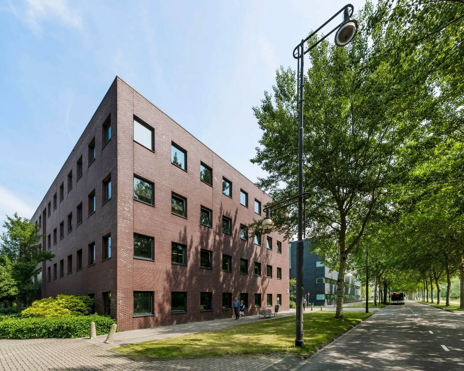 Bakstenen kantoorgebouw met vier verdiepingen aan een boomrijke straat op een zonnige dag.