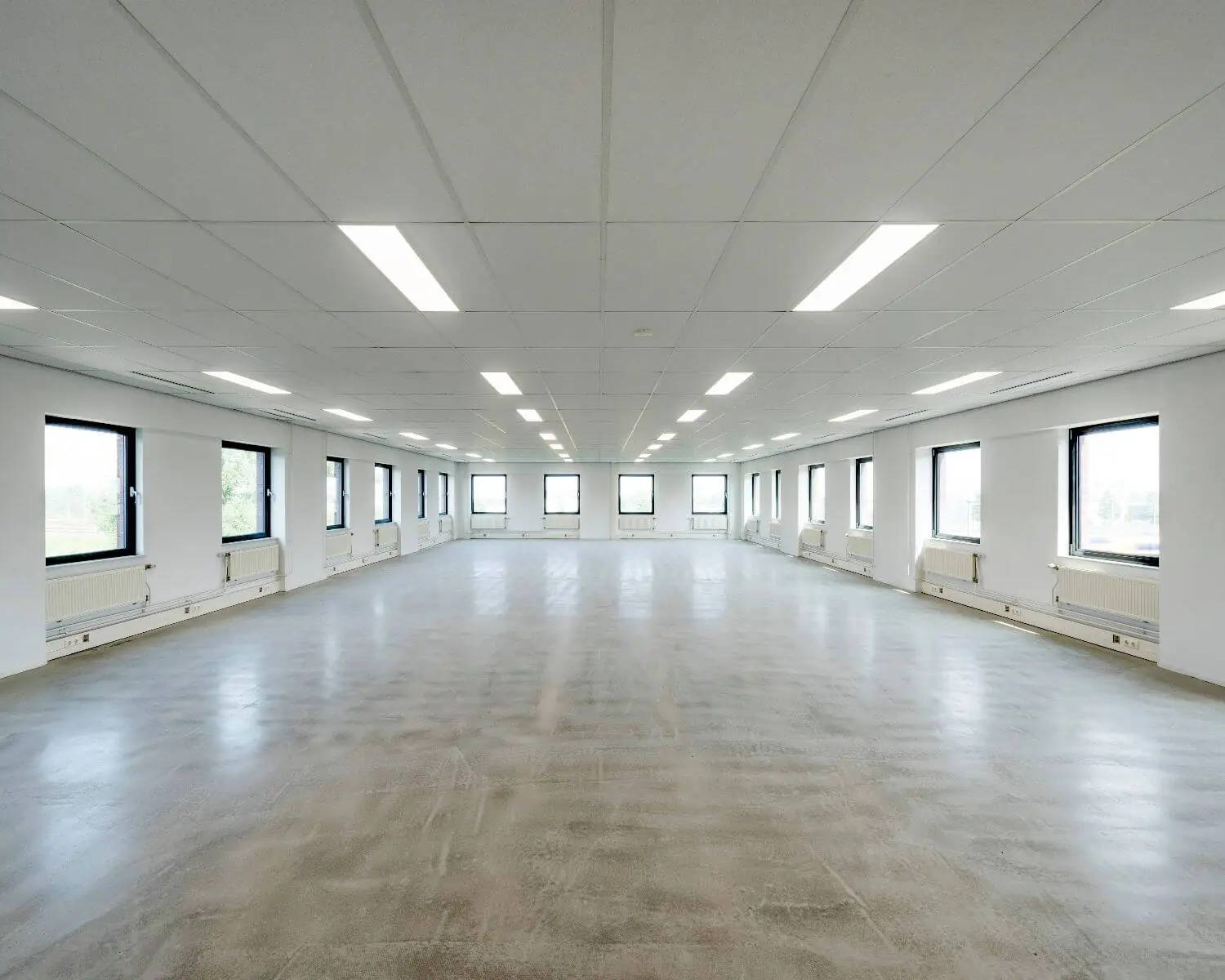 Lege kantoorruimte met wit plafond, betonnen vloer en ramen langs beide zijden.