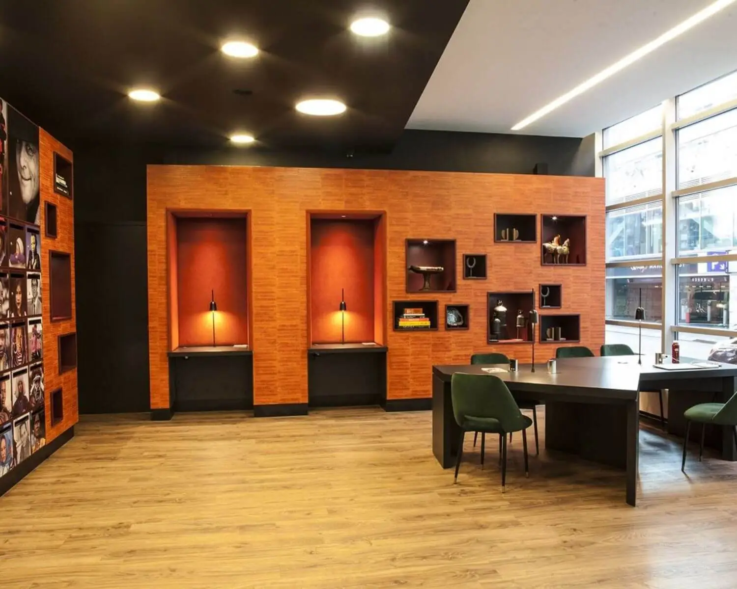 Moderne kantoorruimte met houten vloer, oranje accenten, ingebouwde vitrines en een grote zwarte vergadertafel met groene stoelen.