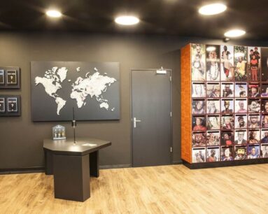 Moderne kamer met wereldkaart aan de muur, een donkere deur, een zwarte tafel en een fotomuur met portretten van mensen uit diverse culturen.
