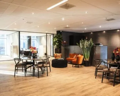 Moderne en sfeervol ingerichte kantoorruimte met zitgedeelte, ronde eettafels en glazen vergaderruimtes.