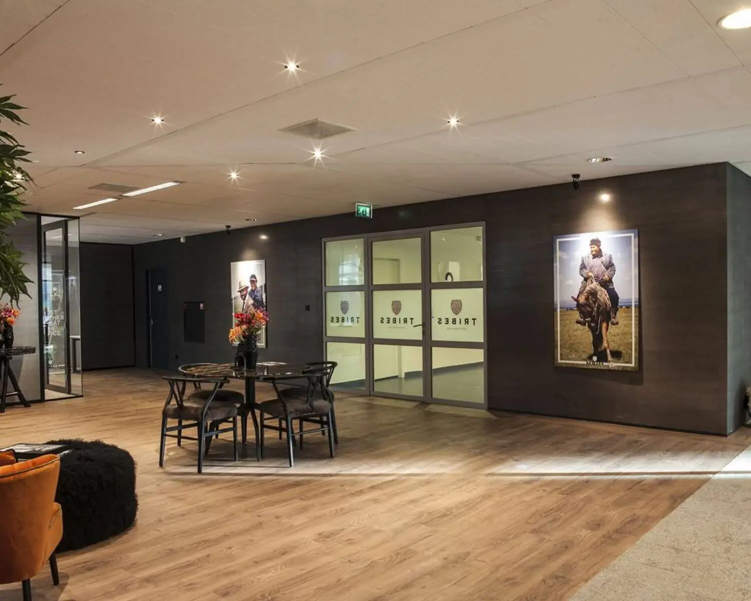 Moderne kantoorlobby met houten vloer, ronde tafel en stoelen, kunst aan de muur en glazen deuren met het logo van Tribes.