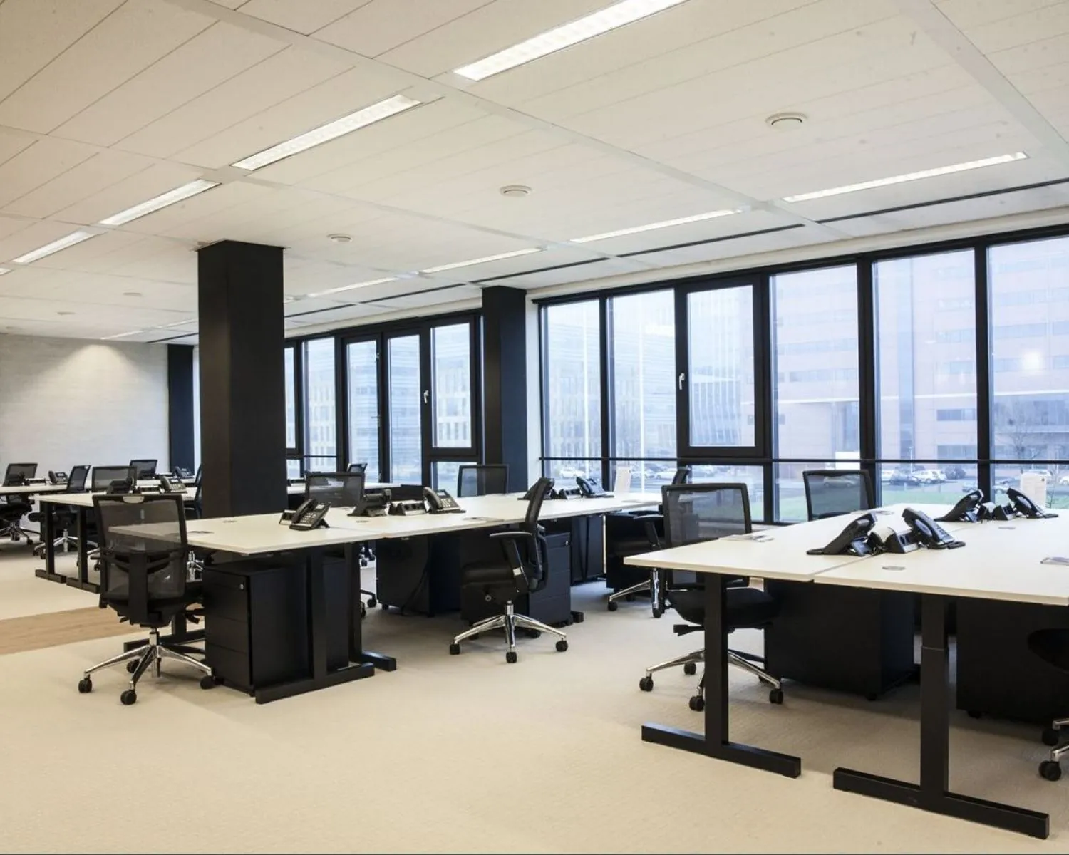 Moderne, open kantoorruimte met meerdere bureaus, bureaustoelen en vaste telefoons bij grote ramen.