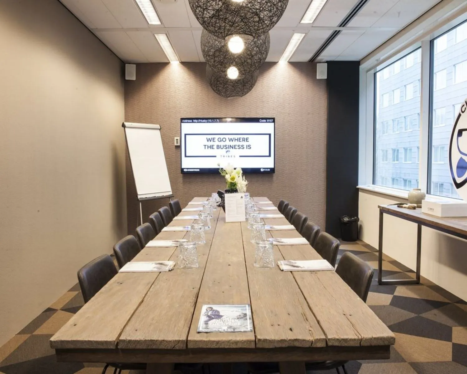 Vergaderruimte met lange houten tafel, zestien stoelen, een scherm met de tekst "We go where the business is", en een flip-over in een moderne kantooromgeving.