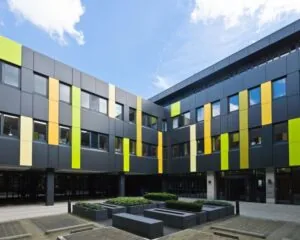 Modern schoolgebouw met gekleurde gevelpanelen in geel, groen en oranje rondom een binnenplein.